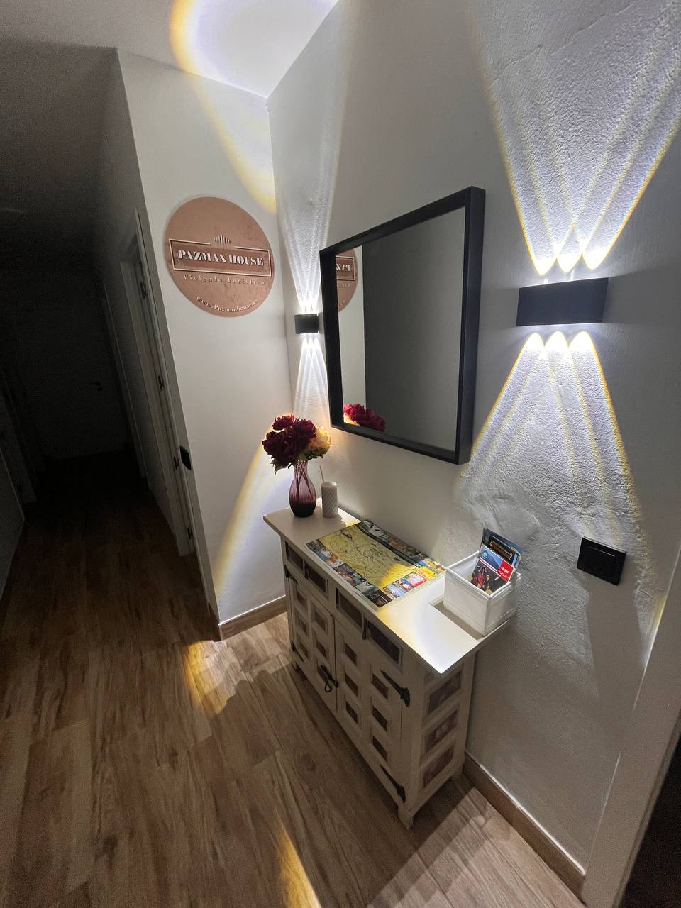 Entrada de PAZMANHOUSE con mueble, espejo y folletos de la sierra